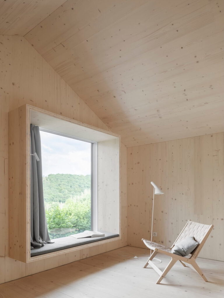 Helle Wohngalerie im Ferienhaus Waldwunder mit gemütlichem Sitzfenster, Lesesessel und Panoramablick auf die bewaldeten Hügel des Westerwalds.